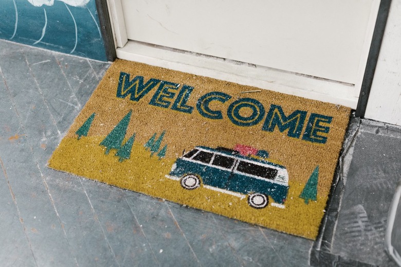 A doormat that says "welcome" and has an image of a camper van and trees.