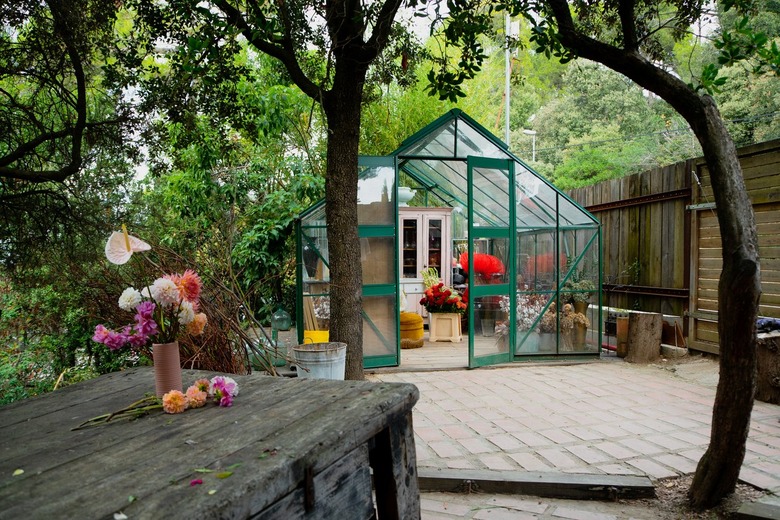 A green greenhouse in a backyard with a wood fence and wood dining table