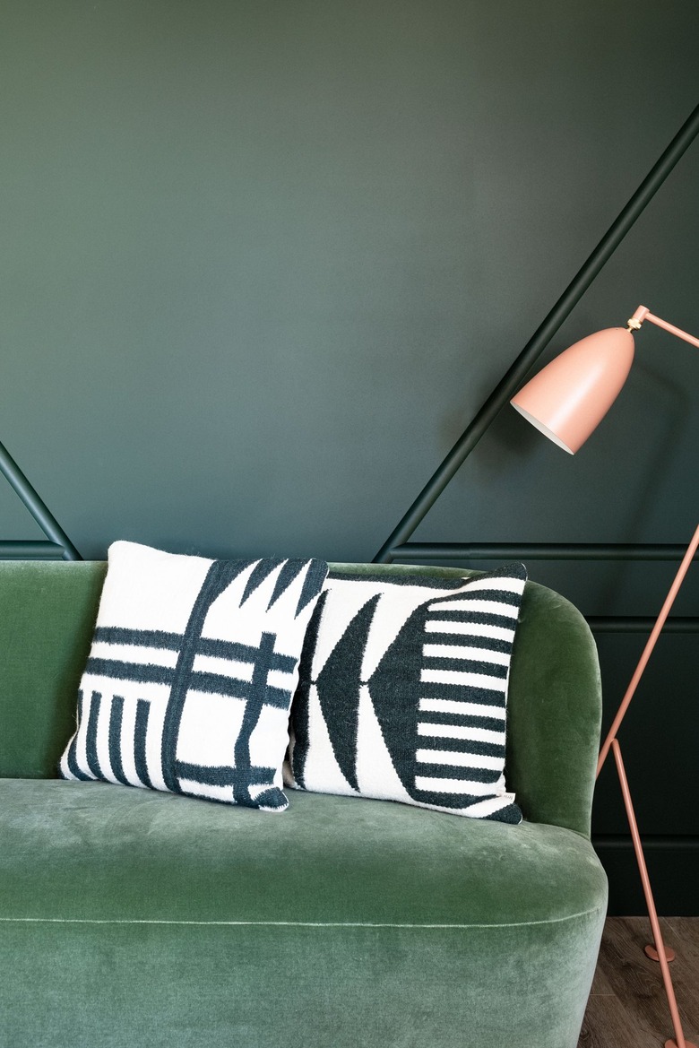 color scheme with a medium-green couch against a dark green wall next to a pink floor lamp