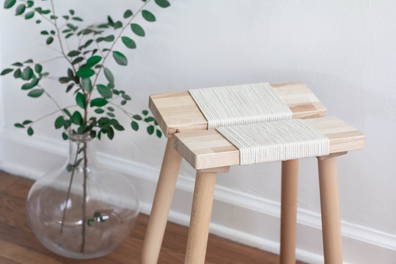 Wood stool with rope next to clear vase with plant