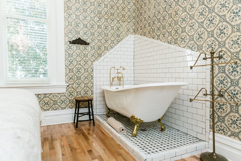 a claw-foot tub sits in a corner of a bathroom on a slightly raised penny tile platform