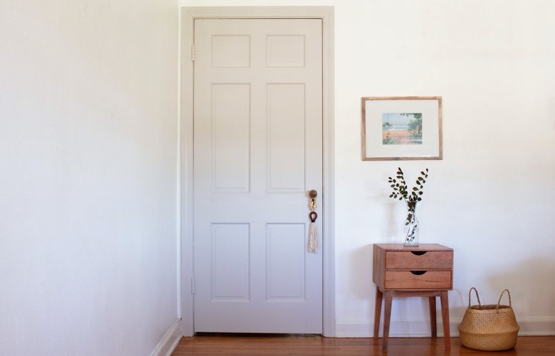 White walled room with wood flooring and wood side table, basket, vase, and art