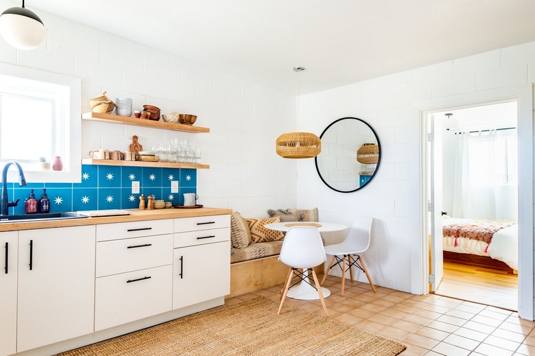 a breakfast nook with a banquette, small round table, a round mirror, and a wicker pendant light