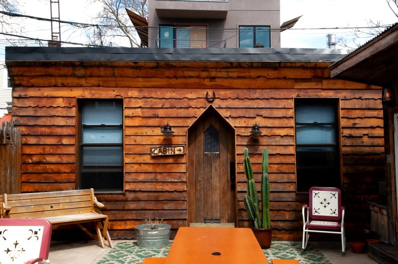 a small wooden cabin with a triangular doorway and an orange picnic bench in front