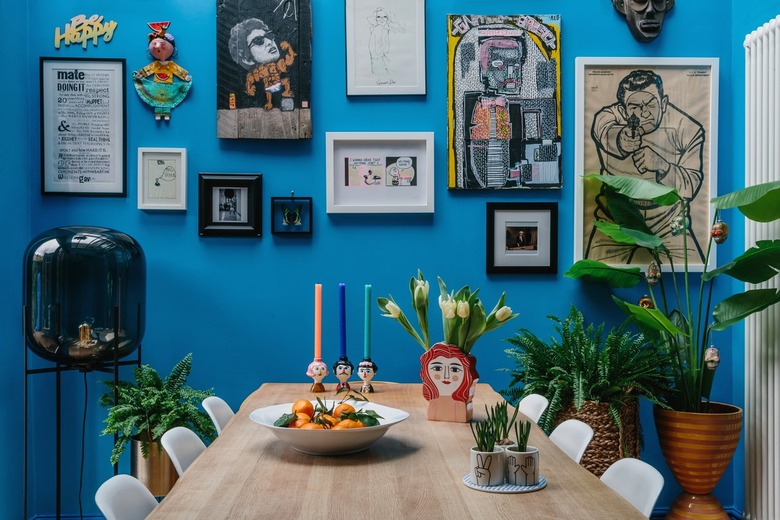 bright blue walls in a dining room with gallery wall art and white molded chairs at a wood dining table