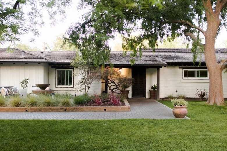 A house with a large tree, and a colorful garden with a fountain.