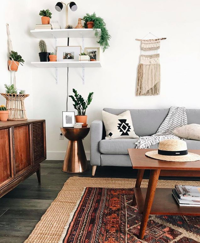 Southwestern-boho living room corner with gray mid-century couch and wooden mid-century coffee table, plus red persian rug layered atop jute rug