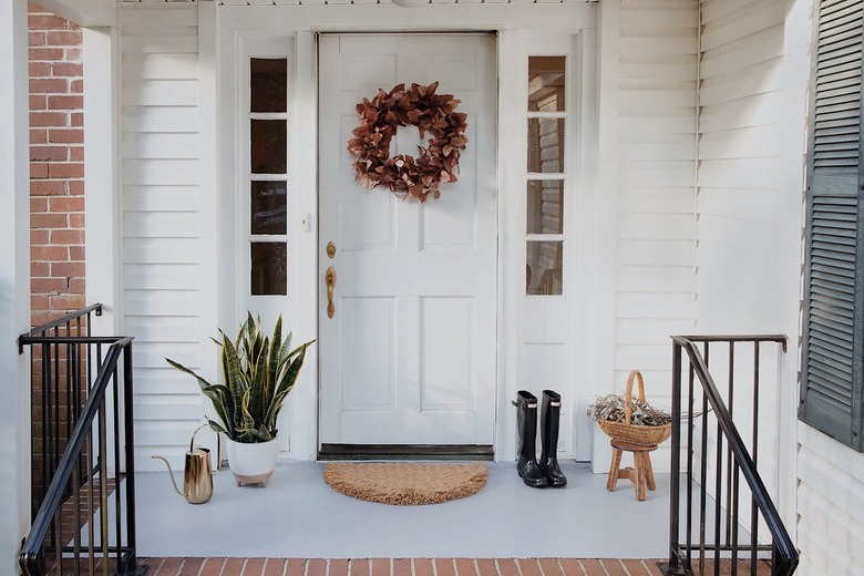 Concrete porch and brick front steps of a white house with a floral door wreath