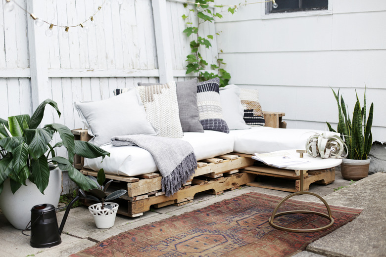 Wood pallet couch on patio with white cushions and throw pillows.