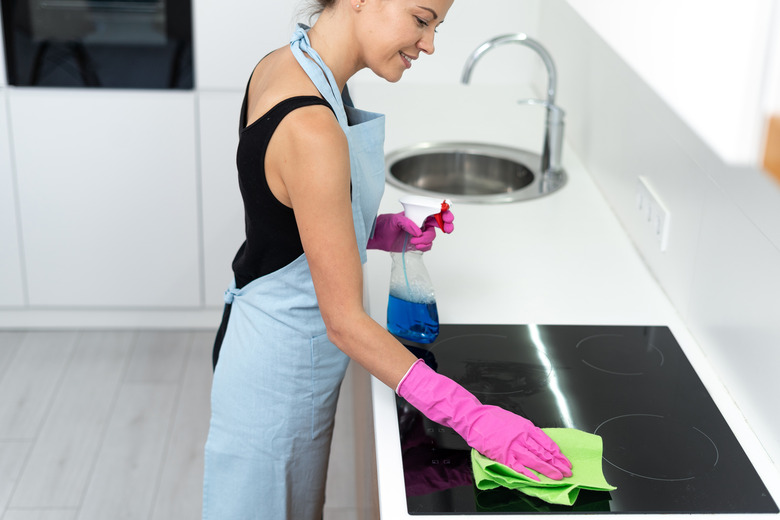 Young adult woman cleaning electric stove in kitchen