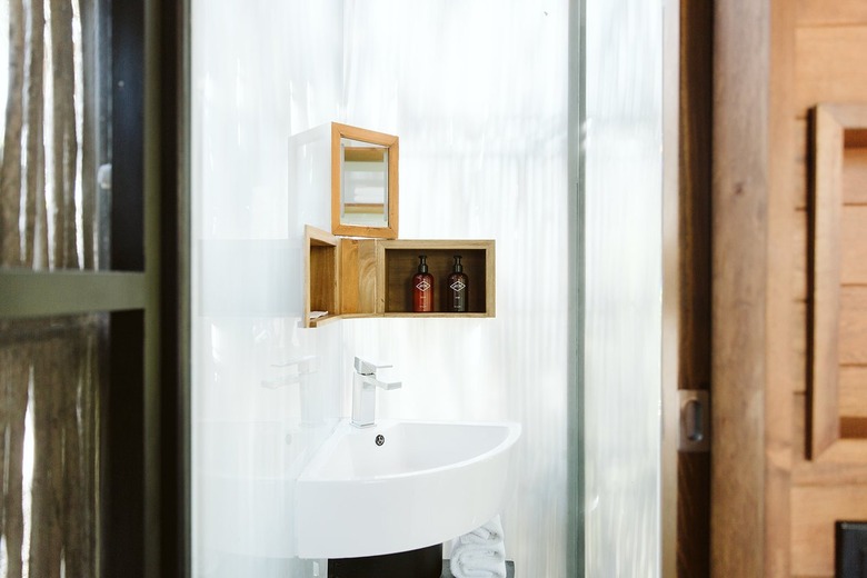 Small corner bathroom sink with small wooden shelves and bath products