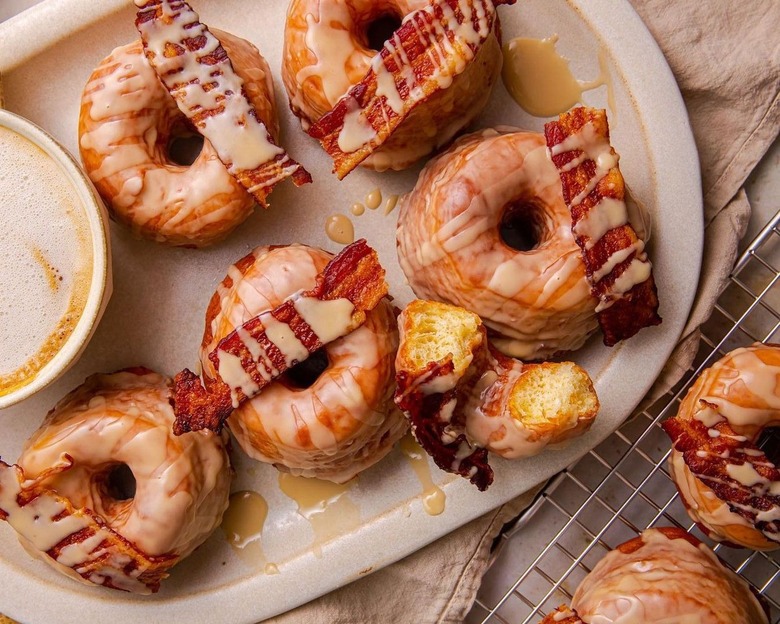 A tray of maple bacon donuts topped with strips of bacon.