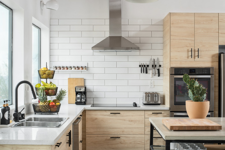 open kitchen with light wood cabinets, silver range hood, white subway tile backsplash, electric stovetop,