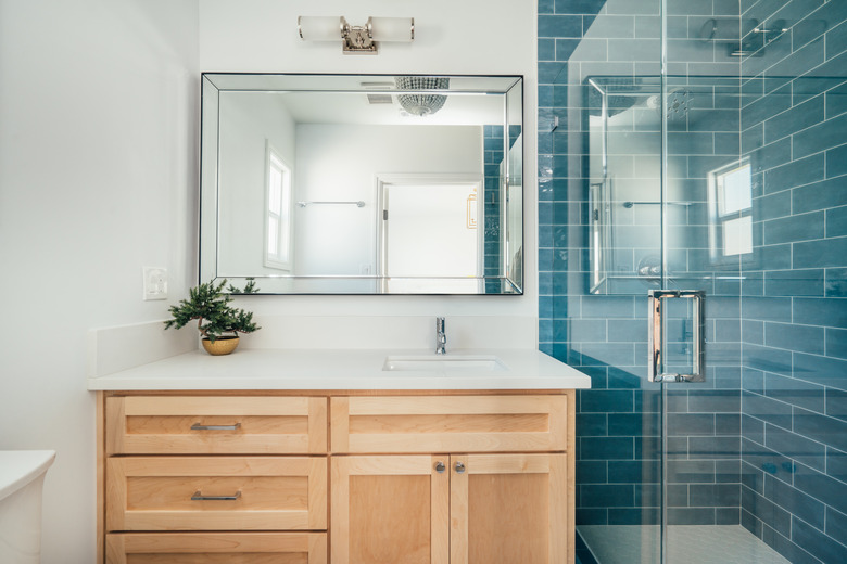 bathroom with teal subway shower tile, glass shower door, light wood bathroom vanity, rectangular mirror with overhead lighting