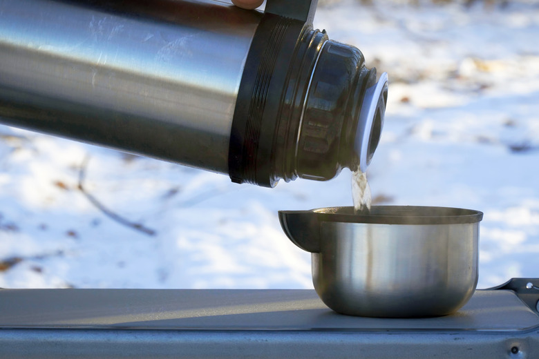 Pours a hot drink from a thermos into a steel mug in winter against the background of snow