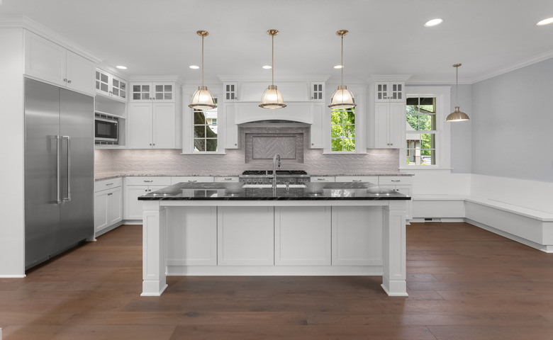 Beautiful kitchen in new luxury home with large island, pendant lights, and hardwood floors. Shows large stainless steel refrigerator.