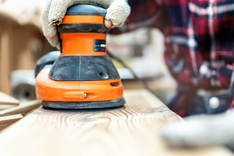 Closeup of carpenter grinding a wood plank with an orbital sander.