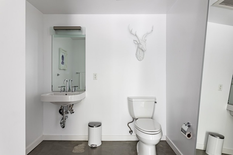 A white bathroom with a wall-mounted sink, a toilet, and a white faux deer hung on the wall