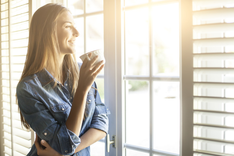 Young woman drinking coffee and looking through window