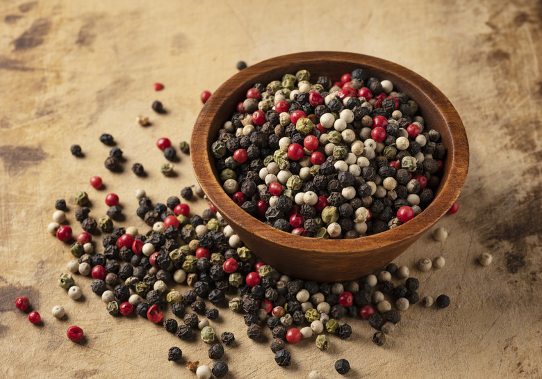 Pepper mix in a bowl. Black, red, white, and green peppercorns on an old cutting board.