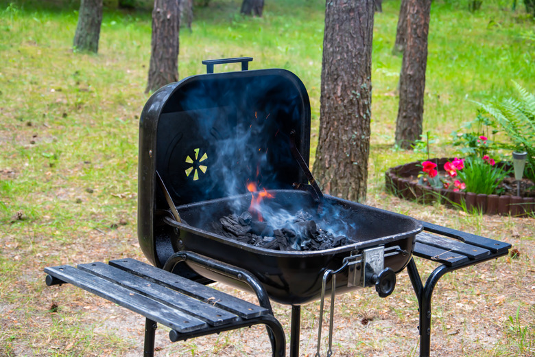 Grilling in backyard - fire, white smoke, smoldering briquettes in grill.