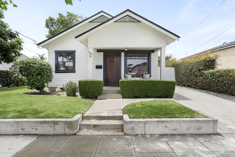 Sidewalk and front yard of a white house with black window frames and dark wood door