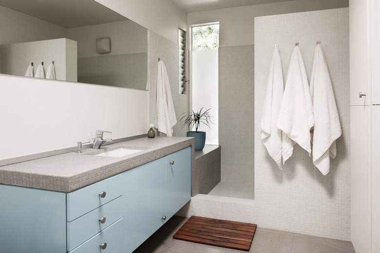 blue and grey bathroom vanity cabinet with sink, walk-in shower and three towels on hooks