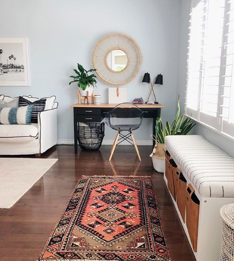 Living room with minimal home office space featuring black writing desk and acrylic midcentury chair with wooden legs