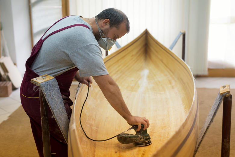 Carpenter with face mask sandpapering wooden canoe