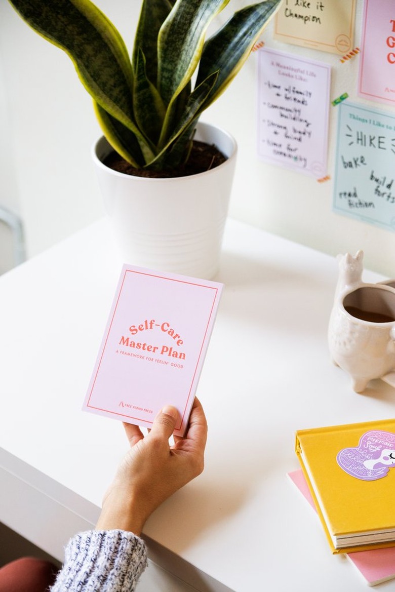 hand holding pink journal over white desk with plant