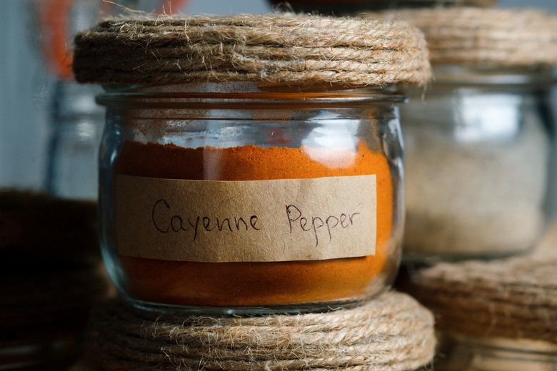 Spices and herbs in glass jars standing in a row on a wooden table or shelf.