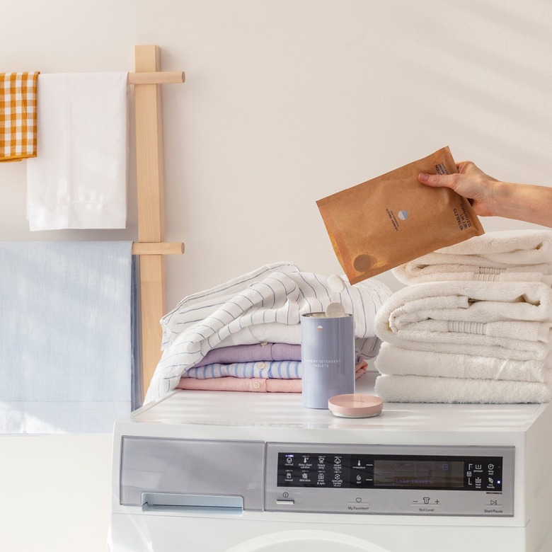 person holding package of blueland laundry tablets near laundry machine