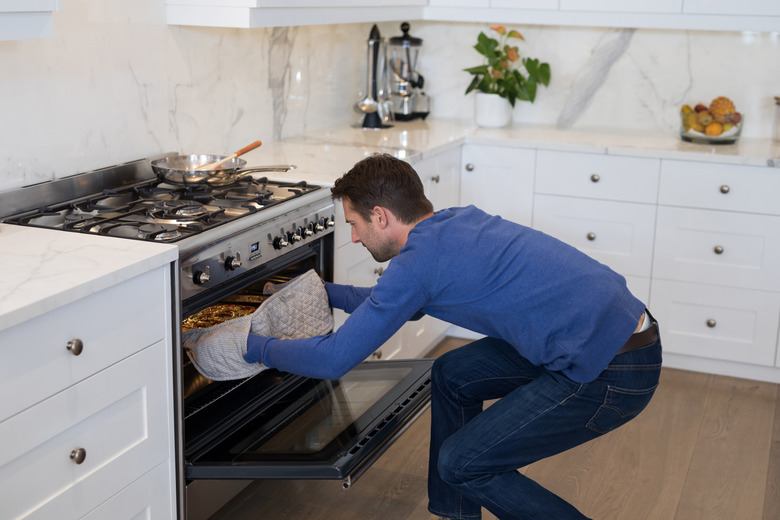 Man putting pizza into oven in kitchen