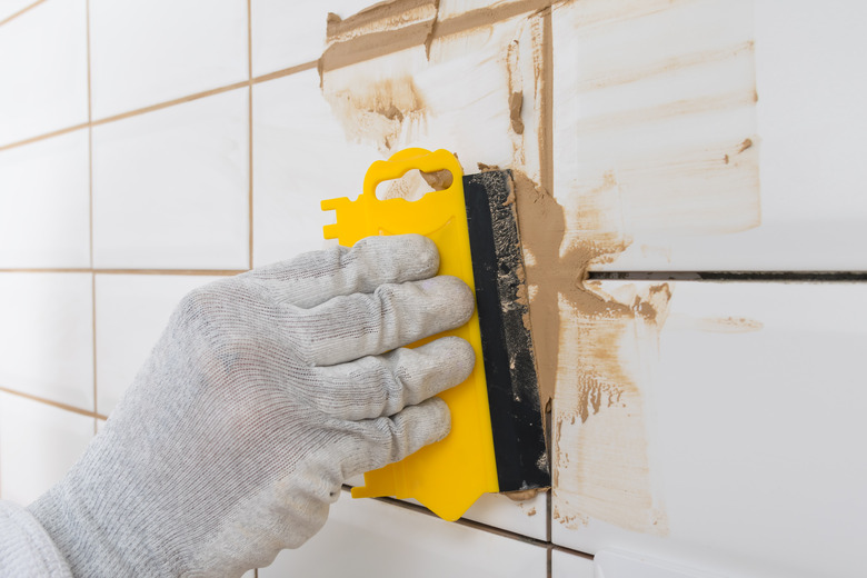 close-up of a yellow trowel, in the process of grout of a white tile, with a light brown sealant