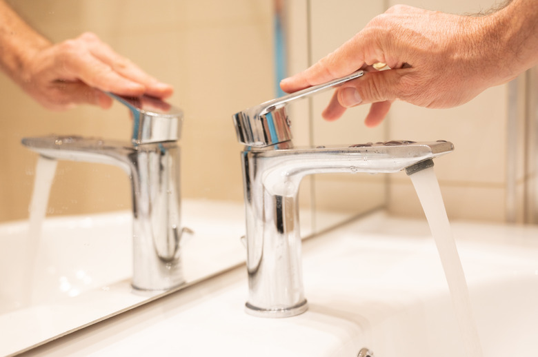 Turning on water faucet in bathroom.