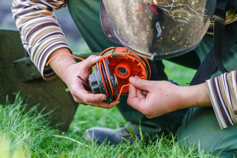 Close up on string trimmer head unknown caucasian man holding and repairing weed cutter replacing parts replacement in day on the field farmer or gardener