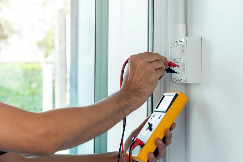 Electrician using a multimeter to measure the voltage at a wall socket.