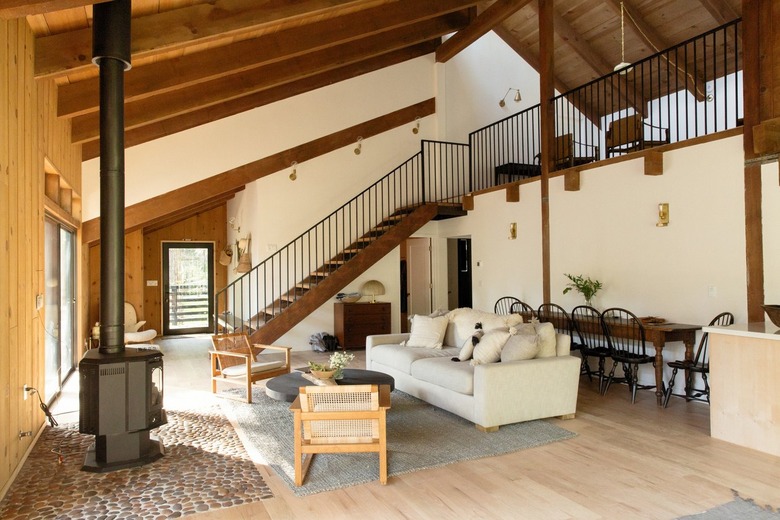 Living room with eclectic furniture, stove fireplace, stone hearth, wood staircase, and slanted wood beam ceiling.