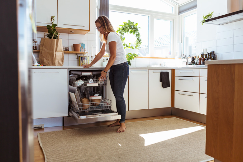 Full length of woman using dishwasher while standing in kitchen