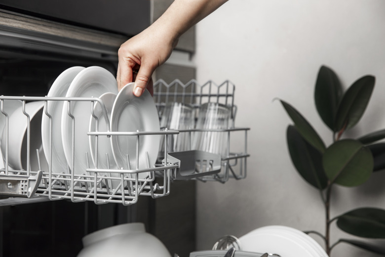 Open dishwasher with clean cutlery, glasses, dishes inside in home kitchen.