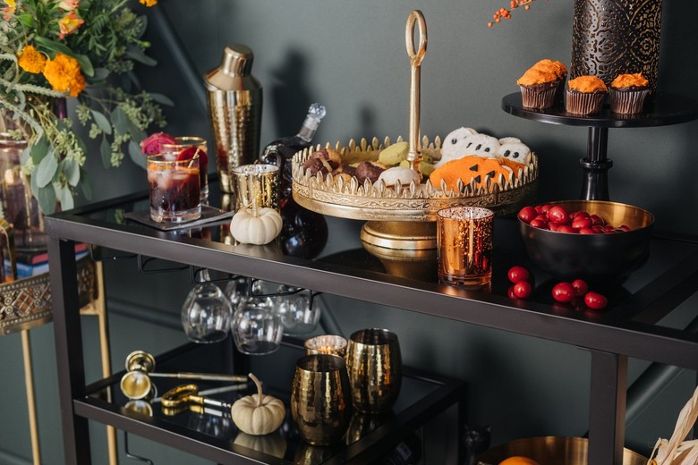 Bar cart with gold cocktail set, cake stand, and autumnal decor