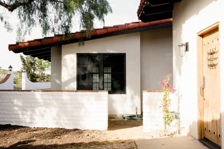 Spanish-style home with white walls and a clay tile roof. A light wood door, a side entrance to the house.