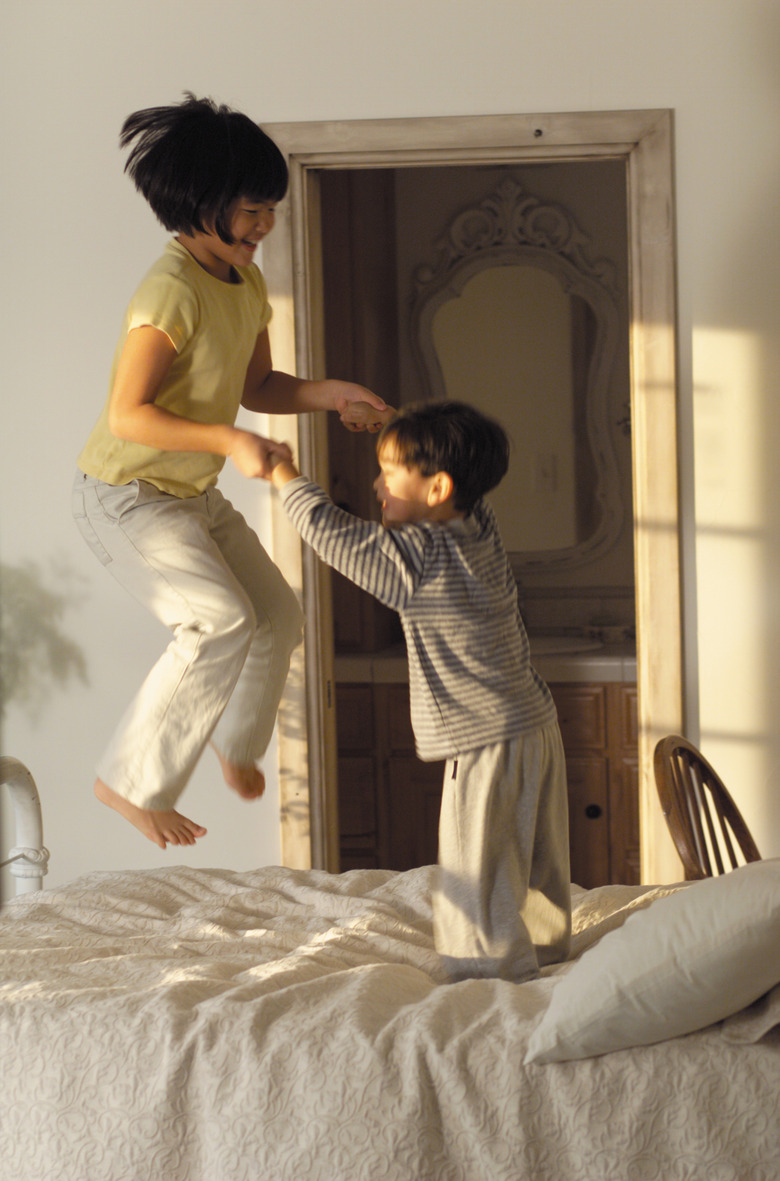 lifestyle photograph of two asian children as they play together and jump on the bed