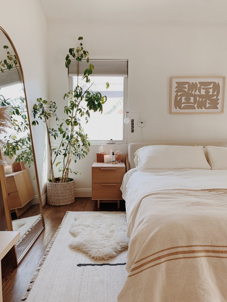 modern fall decor in neutral bedroom with bed and mirror and plant in the corner