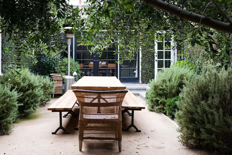 wooden outdoor dining table with benches and rattan chairs outside ivy covered home