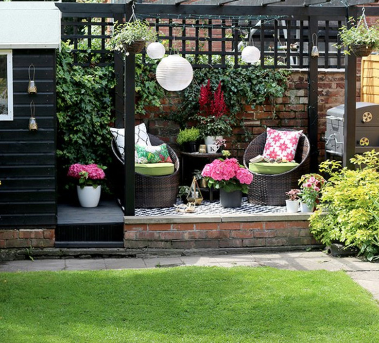 Black wood modern pergola with two wicker chairs, white Chinese lanterns and potted flowers.