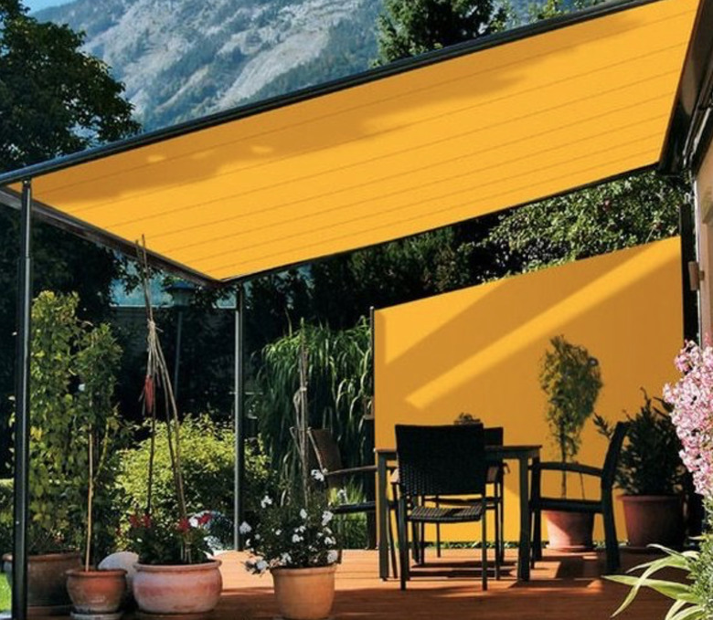 Yellow modern pergola with yellow fabric and black outdoor dining set and potted plants.