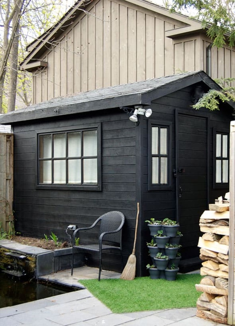 Modern shed painted black with potted plants and black chair