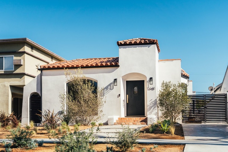 Front yard of a Spanish style white house with terracotta front steps and tile roof