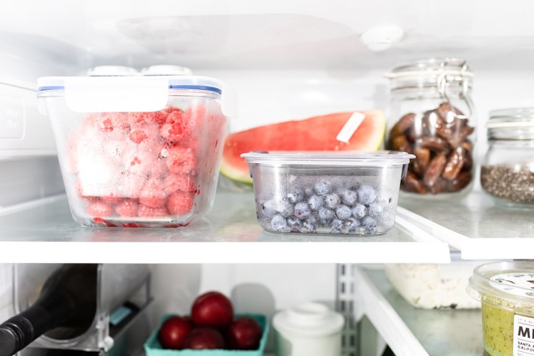 Raspberries and blueberries in clear glass containers on the top shelf in the refrigerator.